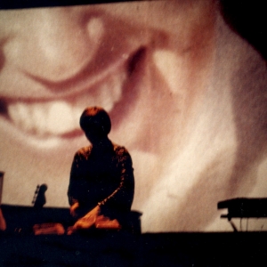 The performer slices grapefruit in front of the projected image of a woman's smiling mouth from a family snapshot