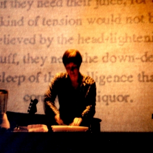 The performers slicces grapefruit in front of a projection screen with words on it