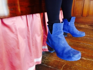 Blue suede ankle boots by John Fluevog, dangle over a 19th century wooden bed with dusky pink silk ruff.