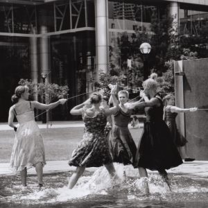 black & white photo: 5 dancers in cocktail dresses in a fountain