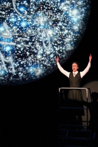 Scientist Lise Meitner played by Andrea Ludwig raises her arms against a backdrop of stars and mathematical equations